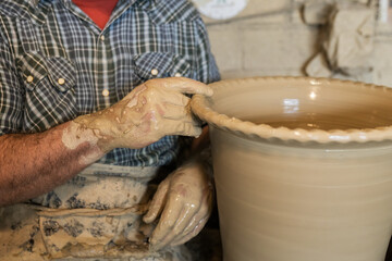 Crop faceless master shaping edge of pot in workshop