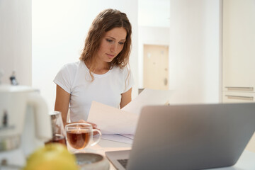 Woman is studying text document while working at kitchen table