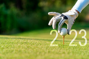 Close up hand Golfer woman putting golf ball for Happy New Year 2023 on the green golf for new...