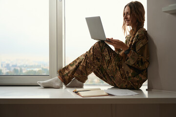 Woman in camouflage uniform uses a gadget on the windowsill