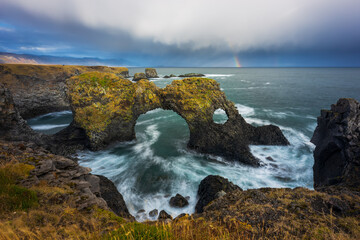 Gatklettur sea arch in Arnastapi, Snaefelsness, Iceland. Cloudy day with a rainbow.