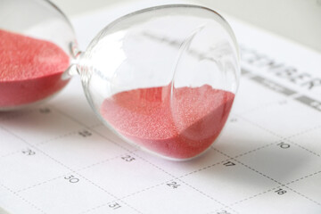 Hourglass with red sand on its side, on calendar, signifying pause in time, time out, taking a...