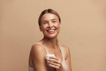 Beauty Woman Holding Face Cream. Closeup Of Female Model With Fresh Skin Laughing with Cream Bottle...