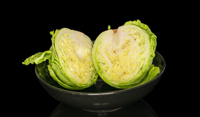 Two halves of a head of cabbage in a black ceramic plate, macro, isolated on a black background.