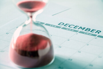 December calendar, with hourglass running out of time and out of focus in foreground, signifying...