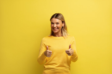 Smiling Woman Showing Big Fingers Isolated. Happy Girl Looking at Camera with Toothy Smile and Showing Thumb Up, Approval Sign, Satisfied with Service, Good Feedback on Yellow Background 