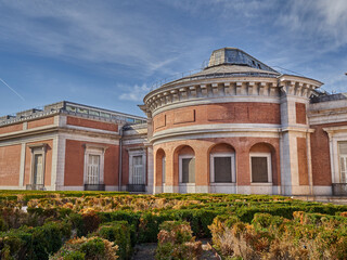 Fototapeta premium View of the back side of El Prado museum brick and stone building with a garden. Museo del Prado opened to the public on 1819 as a Royal Museum of Painting and Sculpture. Madrid, Spain, Europe