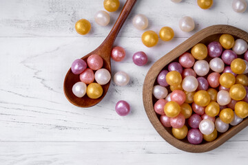 Mixed colorful round candy on white wooden background in wooden plate and spoon. Flat lay, top view. Place for the text.