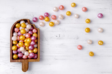 Mixed colorful round candy on white wooden background in wooden plate in the form of ice-cream. Flat lay, top view. Place for the text.