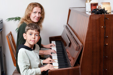 The little boy plays the piano for the first time and is very proud of it, the mother teaches son...