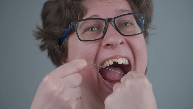 Famale with bad teeth changed her mind late and uses dental floss, but too late her teeth are damaged. Woman with damaged front tooth makes oral hygiene on gray background. Healthcare.