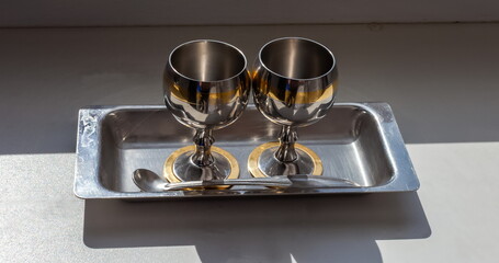 Metal glasses and a spoon on a tray close-up on the background of the window sill