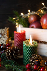 Fototapeta na wymiar Red and green candle made of natural honeycomb on a wooden table. Red berries, cones and spruce branches in the background. Dark wooden background