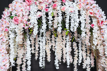 white metal arch with artificial flowers on the photo zone. white flowers on a wedding photo zone against a black background. ready-made photo zone for a wedding photo shoot with artificial flowers