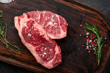 Two steak raw striploin (New York) of beef on a board with seasoning, salt and red pepper. Fresh meat for grilling