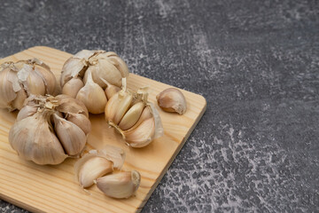 Fresh raw garlic on cutting board display with fork and spoon on dark background for cooking concept set up