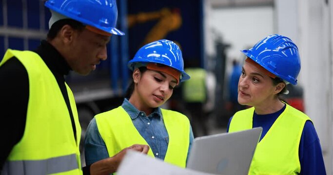 Multiethnic engineers working inside robotic factory while using computer laptop