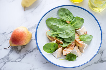 Plate with fresh spinach, grilled pear and camembert salad, high angle view on a white marble background, horizontal shot