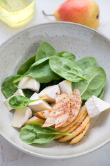 Salad with fresh spinach leaves, pear and camembert cheese slices served in a beige plate, vertical shot, close-up