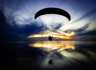 Powered paraglider walking over lake during sunset.