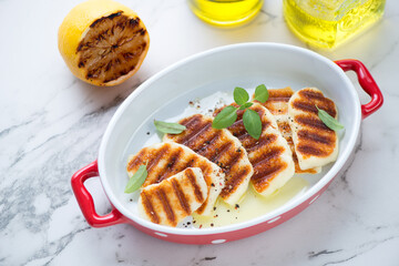 Red serving pan with grilled halloumi cheese, elevated view on a white marble background, horizontal shot