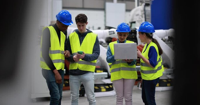 Multiracial engineers working inside robotic factory using computer laptop and mobile phone