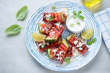 Grilled watermelon with grated cheese and yogurt on a blue and white plate, elevated view on a grey granite background, studio shot
