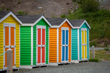 Fototapeta na wymiar A row of small colorful painted huts or sheds made of wood. The exterior walls are colorful with double wooden doors. The sky is blue in the background and the storage units are sitting on gravel. 