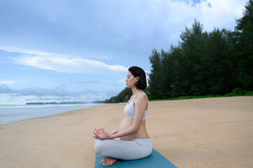 Fototapeta na wymiar Pregnant woman practices yoga and meditation while doing lotus poses and sits on the peaceful beach with a nature scene- Healthy lifestyle concept