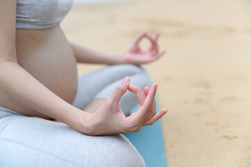 Close up pregnant woman hands practices yoga in lotus pose and sits on the peaceful beach with nature scene- Healthy lifestyle concept