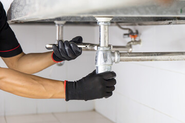 Technician plumber using a wrench to repair a water pipe under the sink. Concept of maintenance,...