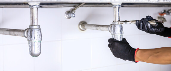 Technician plumber using a wrench to repair a water pipe under the sink. Concept of maintenance,...