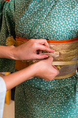 Japanese woman's hands tying obijime around the obi during traditional kimono dressing