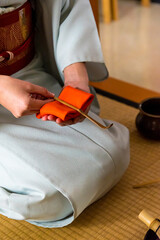 Japanese woman, tea master, Sen Rikyu, hands using an orange purifying cloth to clean a chashaku...