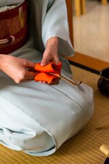 Japanese woman, tea master, Sen Rikyu, hands using an orange purifying cloth to clean a chashaku bamboo matcha tea spoon in Japanese traditional tea ceremony © A Certain Aesthetic