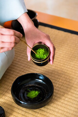 Japanese woman, tea master, Sen Rikyu, hands placing matcha powder into chawan tea bowl during a...