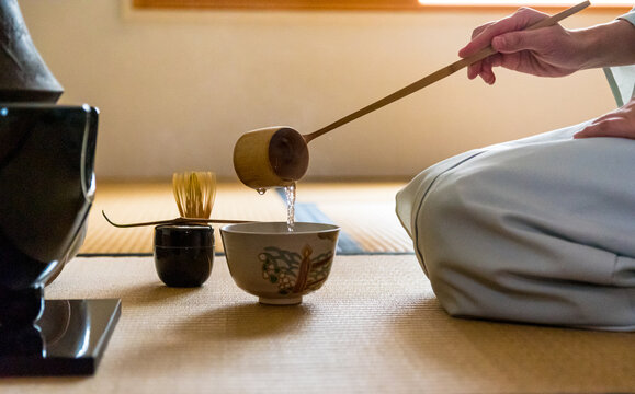 Side view of Japanese woman, tea master, Sen Rikyu, hands using a Hishaku bamboo ladle to pour hot water into chawan tea bowl filled with matcha powder during a Japanese traditional tea ceremony