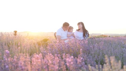 Beautiful young family dad and mom with little girl sitting on picnic at sunset in lavender field.