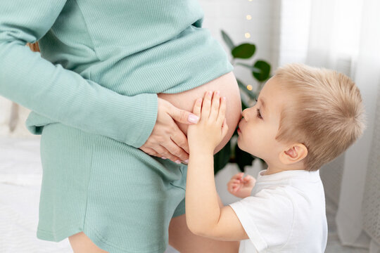 close-up of a pregnant woman's big belly and a baby kissing mom's belly, the concept of waiting for a child, love and parenting