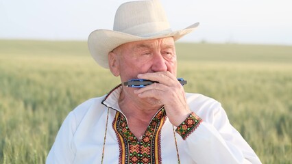 An old Ukrainian grandfather plays the harmonica, he is dressed in an embroidered jacket.