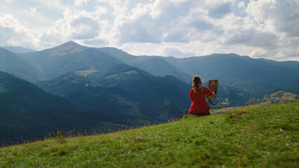 Unknown woman painting masterpiece on green hill. Girl drawing on easel outdoors