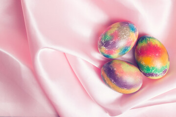 Colorful Easter eggs on a smooth pink silk texture. Top view, flat lay.