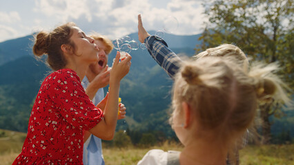 Family playing blowing soap bubbles in summer mountains. Parents amusing kids.