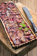 Traditional German zwetschgenkuchen with sliced plums and herbs served as close-up in a backing form on a black board
