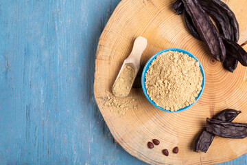Carob pods and carob powder over a blue wooden background. Top view.