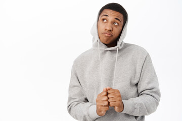 Portrait of African american muscline man looking thoughtful and silly, pull hoodie on head, staring aside, standing over white background