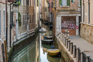 Fototapeta na wymiar Small, Venetian canal, located off the main areas of Venice. Small boats can be seen moored against the doors opening up to the water
