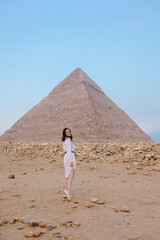 woman is photographed in front of the pyramids in Cairo. Tourist trip to Egypt. Excursion to the wonder of the world. Incredible emotions of happiness and delight. chidhood dream. Girl in desert Giza - obrazy, fototapety, plakaty