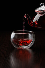 Pouring tea into a glass thermos cup from a glass teapot on a black background. Selective focus.