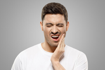 Young guy with closed eyes suffering from severe toothache, touching jaw to ease strong tooth pain